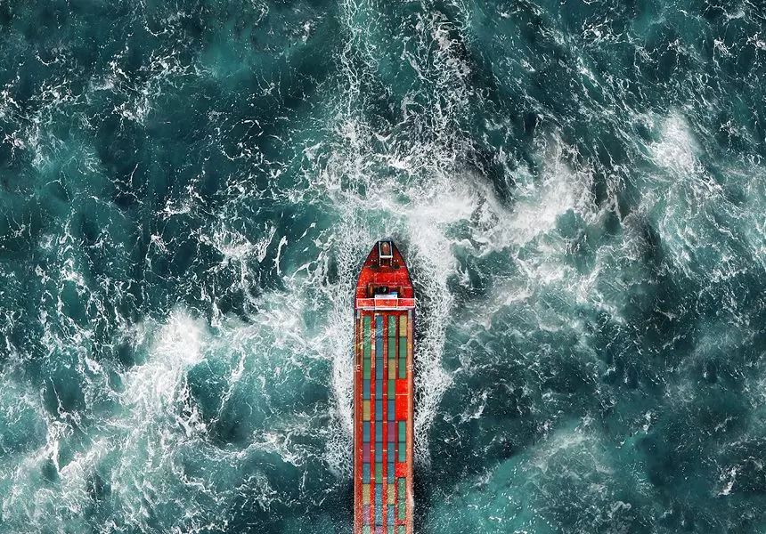An aerial photo shows a cargo ship loaded up with colorful containers on a choppy sea.